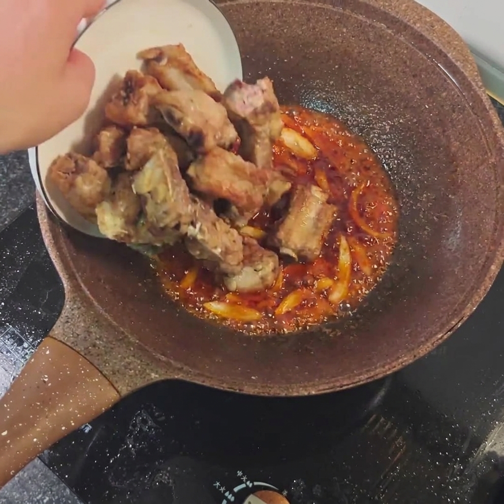 Pan-fried pork ribs being mixed with spicy sauce and aromatics in a pan.