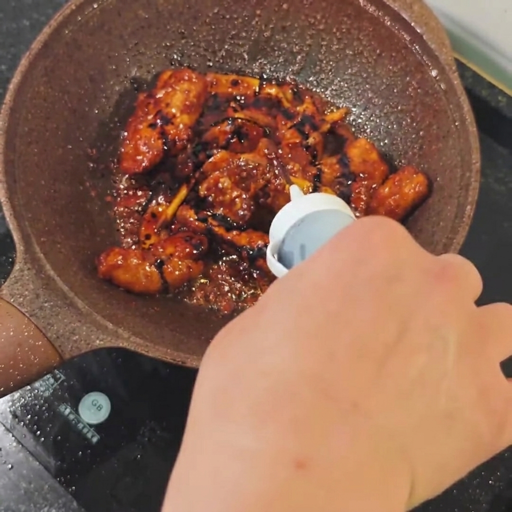 Dark soy sauce being poured from a small bottle into a pan of browning pork ribs.