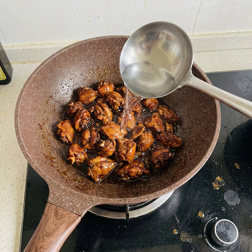 Water being poured from a ladle into a pan filled with browned pork ribs.