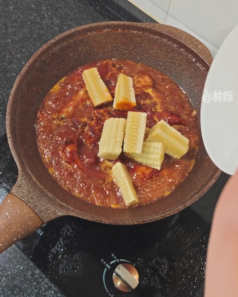 Pieces of fresh corn being added to a pan of simmering pork ribs in a spicy sauce.