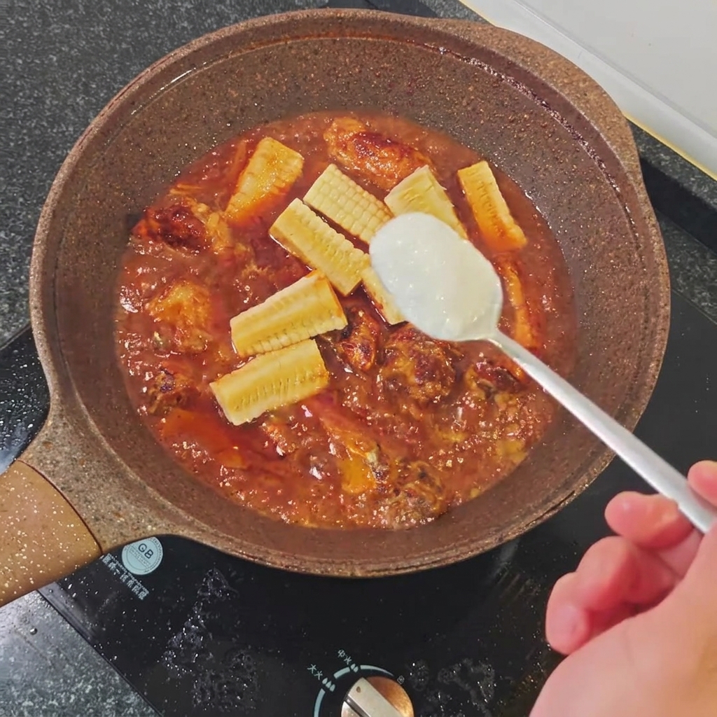 A spoonful of white sugar being added to the simmering braising liquid in the pan.