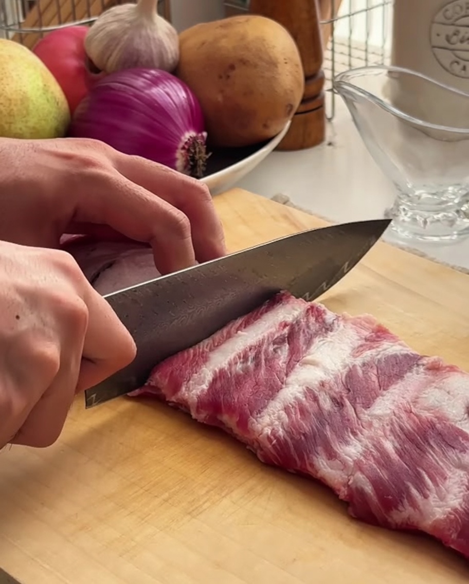 A close-up view of a chef using a sharp knife to portion a rack of pork ribs on a wooden board.