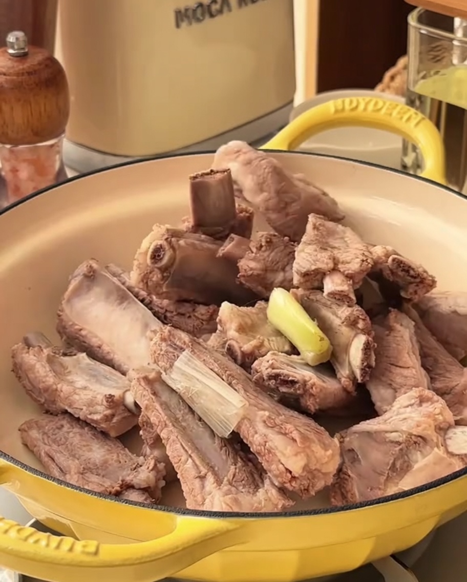 Spicy marinade being poured over blanched pork ribs in a cooking pot.
