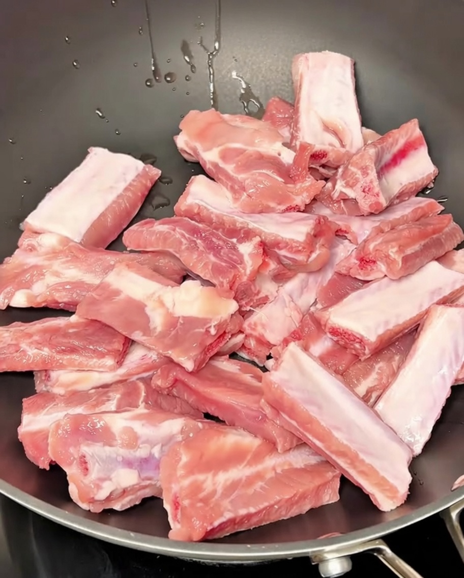 Pork ribs simmering in a pot of water with aromatics during the blanching process.
