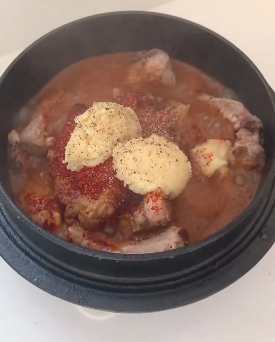 Chopped white onions and green onion slices added on top of the seasoned pork ribs in a pot.