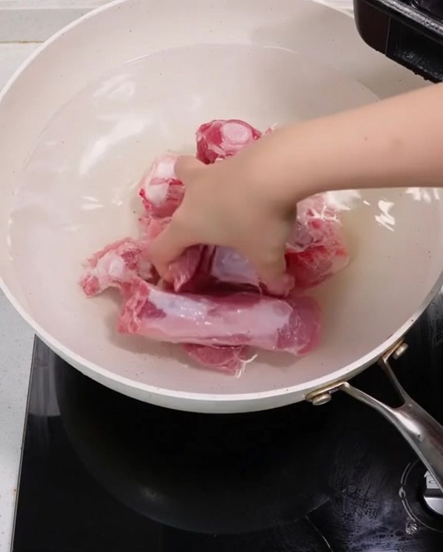 Pork ribs boiling in a pot with green onions and ginger slices for blanching.