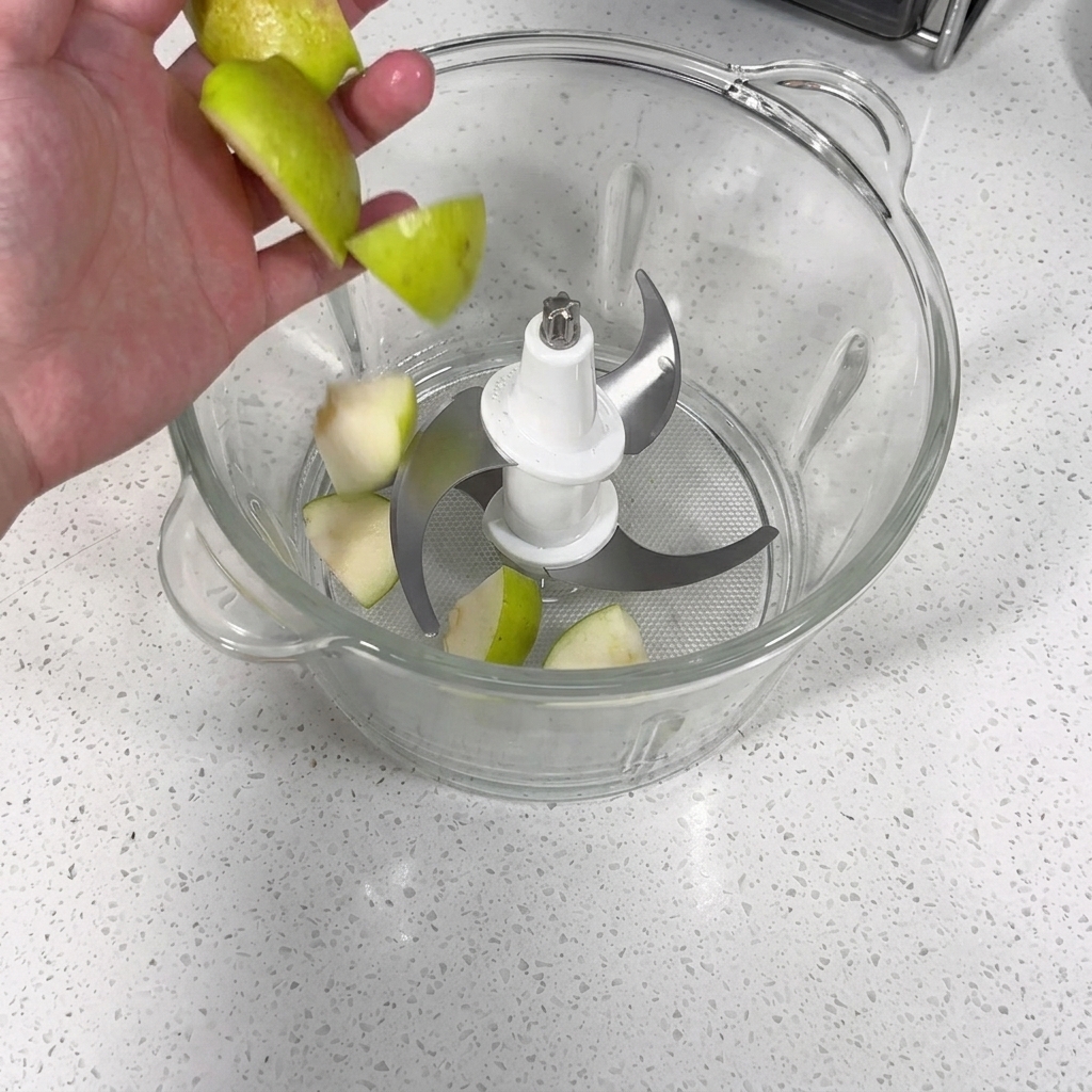 A food processor filled with pieces of apple, pear, garlic, and onion being blended into a puree.