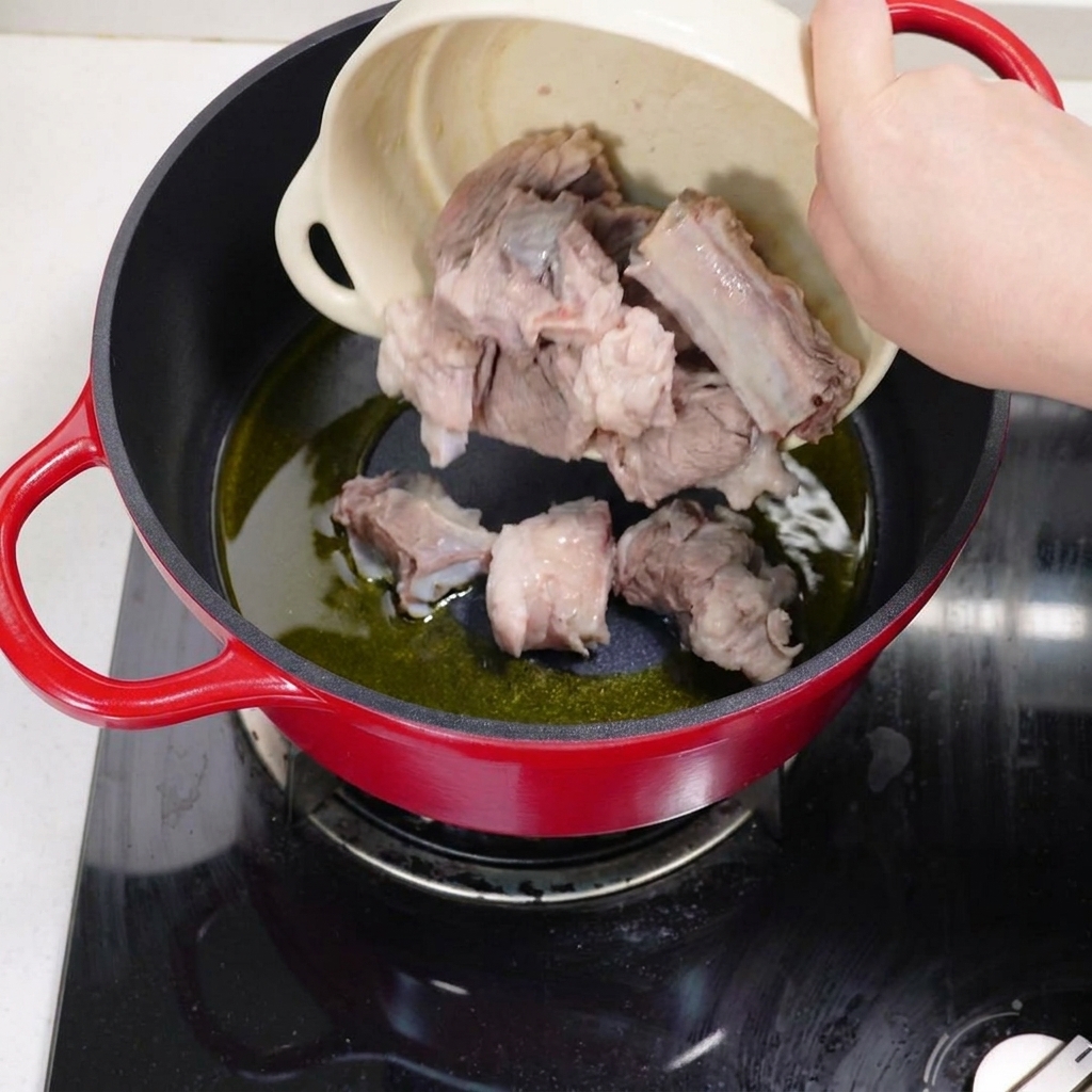 Blanched pork ribs being stir-fried in a pot with hot oil until they turn brown.