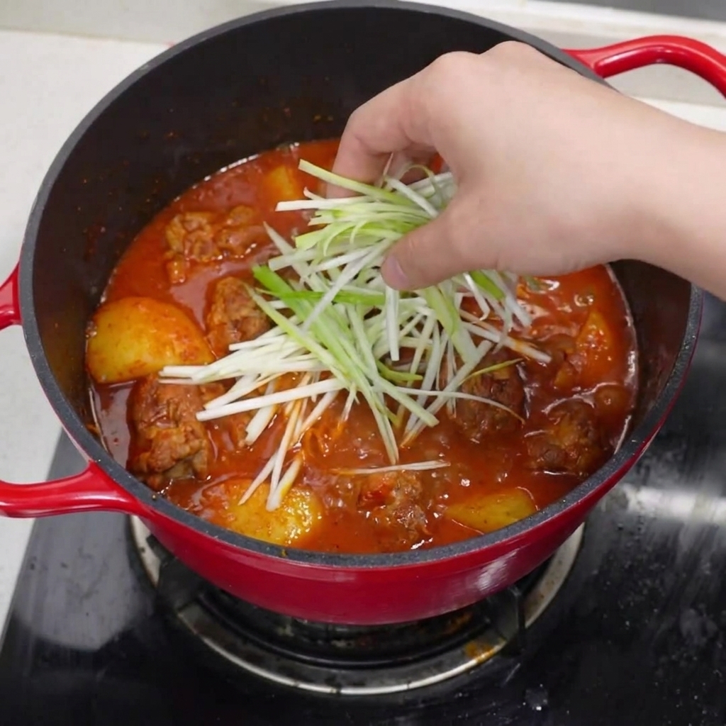 The finished pot of braised pork ribs, topped with vibrant green onions, red chili slices, and a dusting of black pepper.