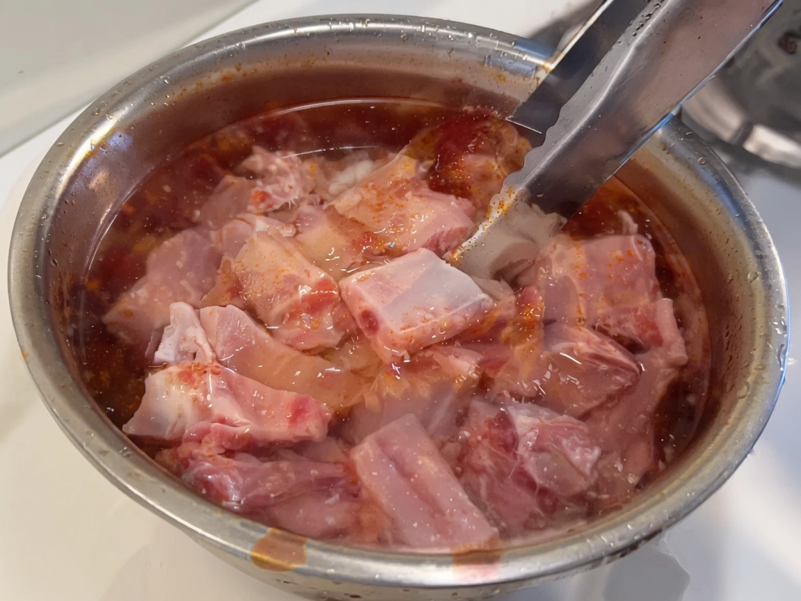 Fresh raw pork ribs submerged in a bowl of clear water.