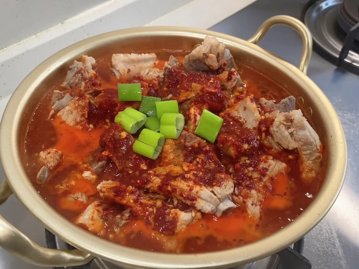 Pot of braising ribs being topped with fresh chopped green onions.