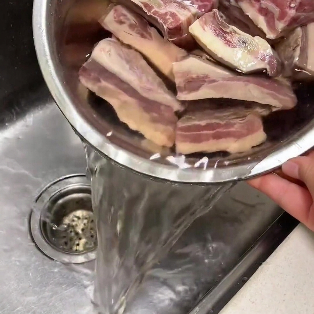 Beef ribs soaking in a bowl of cold water in a kitchen sink.