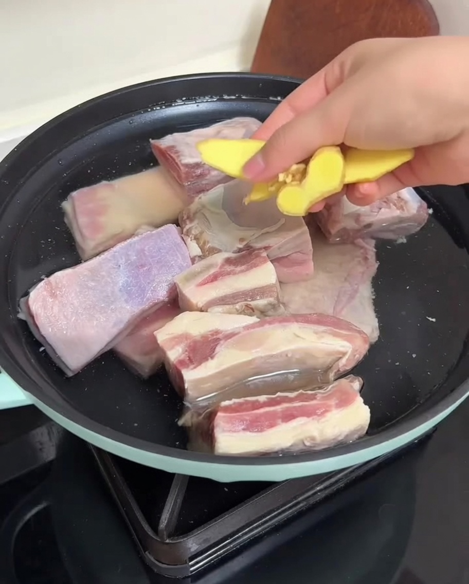 Beef ribs in a pan with water and ginger slices being prepared for blanching.