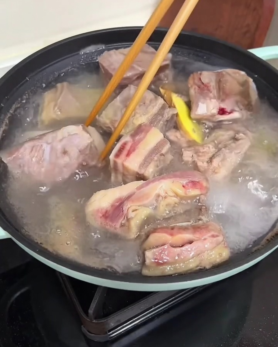 Hands using chopsticks to clean blanched beef ribs under running water.