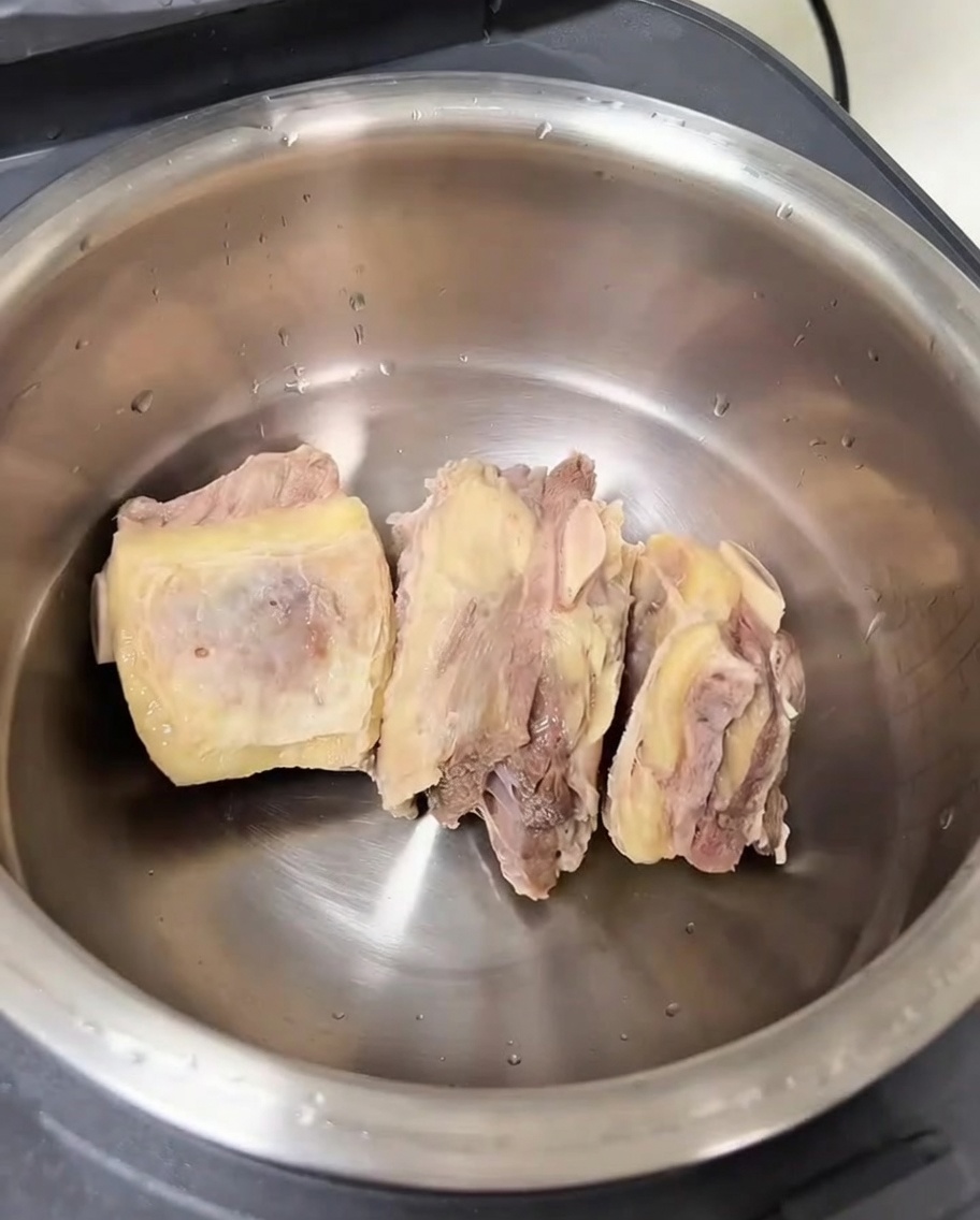 The inner pot of a rice cooker containing cleaned beef ribs and various aromatics.