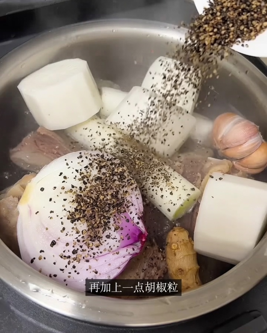 Hot water being poured into the rice cooker over the beef and aromatics.