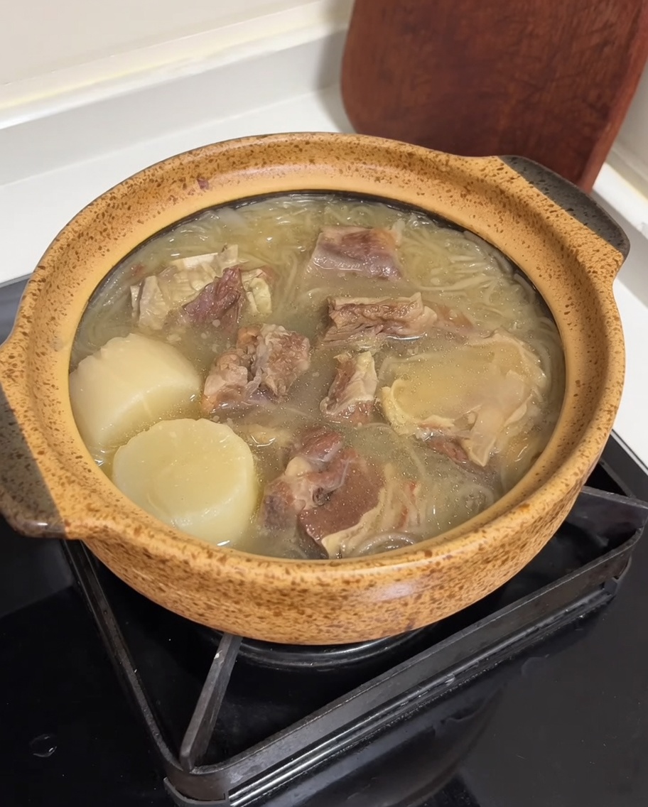 A ceramic pot filled with beef soup, topped with bright yellow egg strips and vibrant green sliced onions.