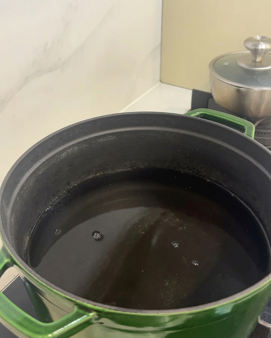Pieces of raw beef short ribs inside a large green pot filled with cold water.