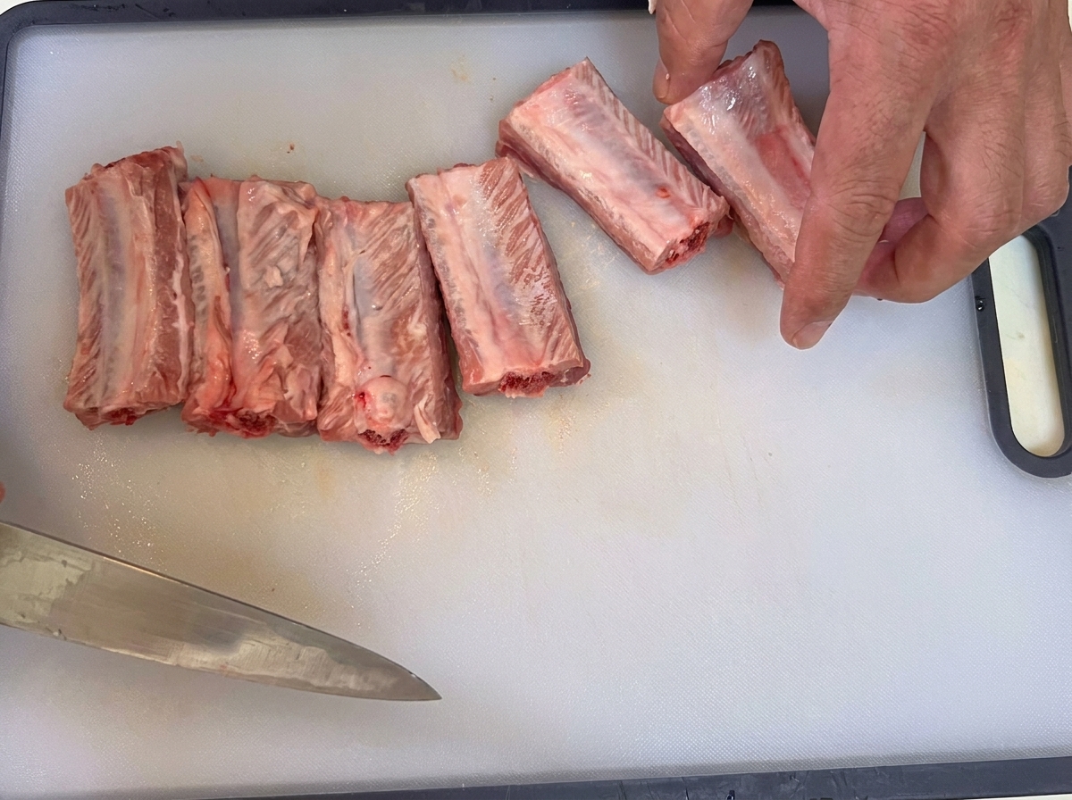 A knife peeling the thin connective tissue off the back of raw pork ribs.