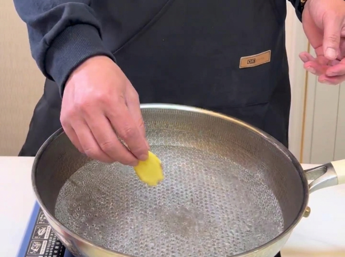 Slices of ginger being dropped into a pot of boiling water for blanching.