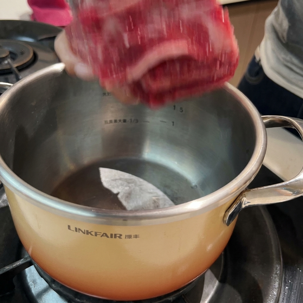 Beef ribs soaking in a pot of cold water with aromatics, ready for the blanching process.