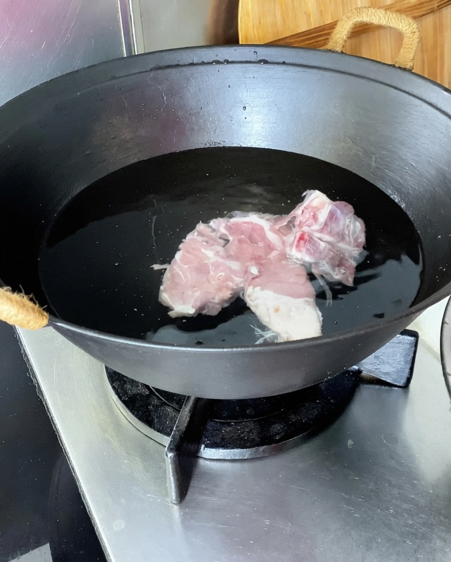 Pork spine in a wok of cold water with ginger, scallions, and cooking wine.