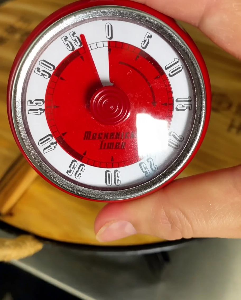 A kitchen timer set to one hour with a simmering pot in the background.