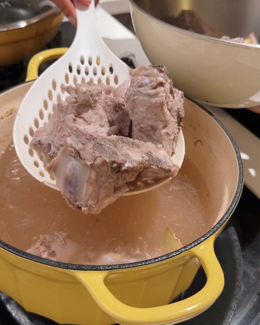 Strainer lifting blanched pork spine pieces out of a pot.
