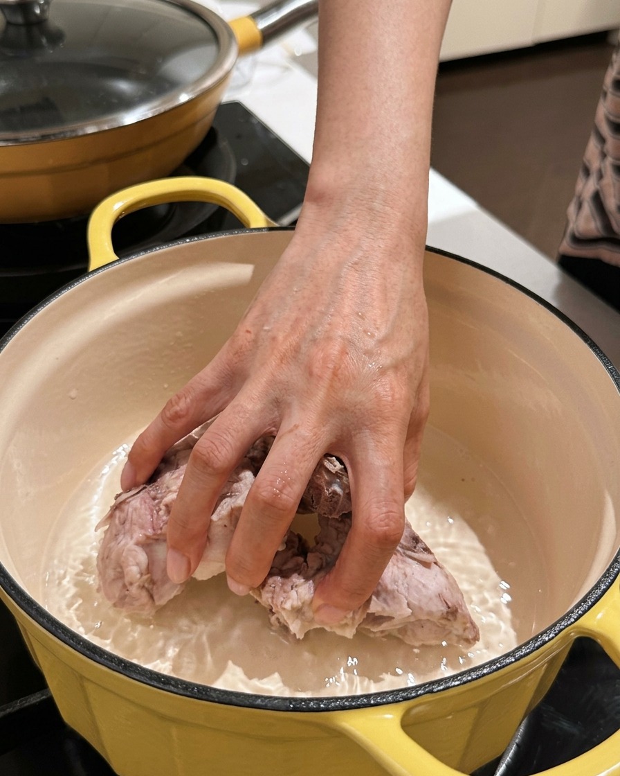 A hand placing cleaned pork spine pieces back into an empty braising pot.