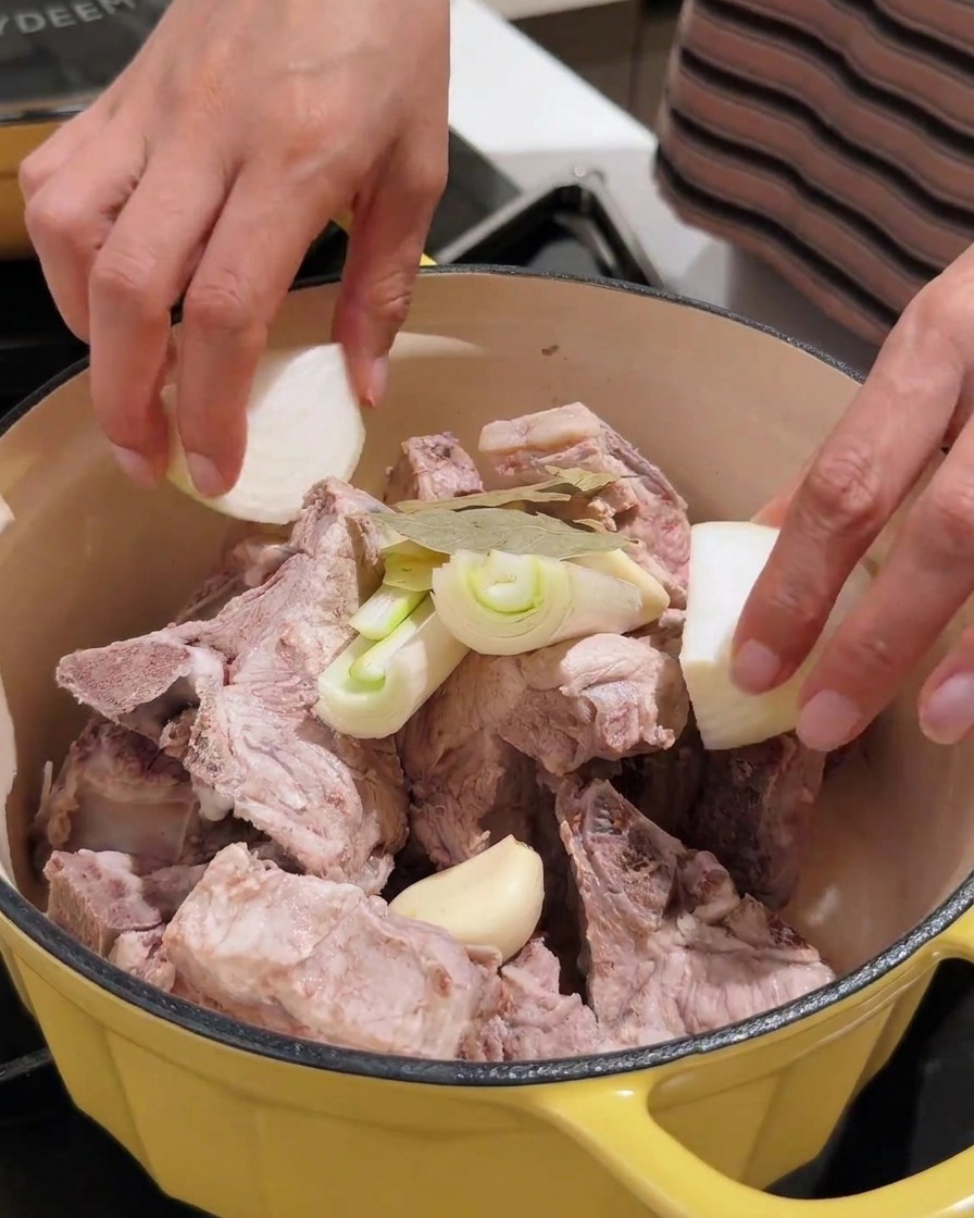 Various aromatics including garlic, onion, and soybean paste being added to the pot with pork.