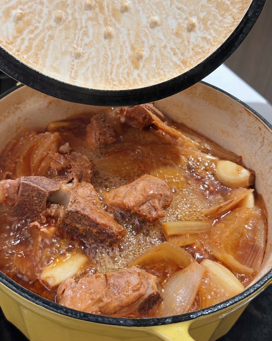 A pot of bubbling braised pork ribs with rich broth as the lid is lifted.