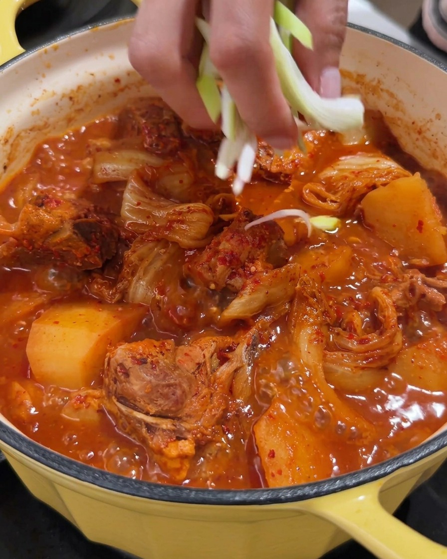 A vibrant pot of spicy pork spine soup being garnished with fresh chopped scallions.