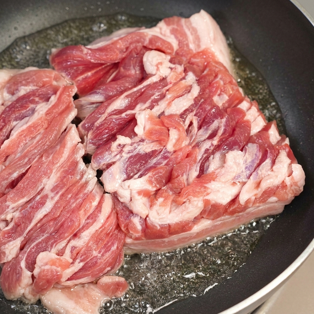 A pan with sizzling pork belly and a spoon removing excess rendered fat.