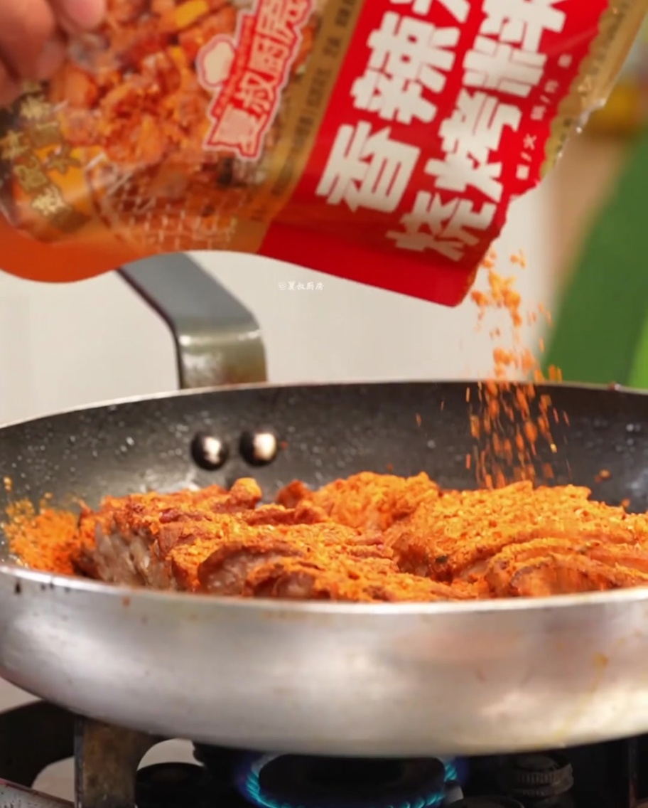 Pork being seasoned with spices and aromatics in a hot pan.