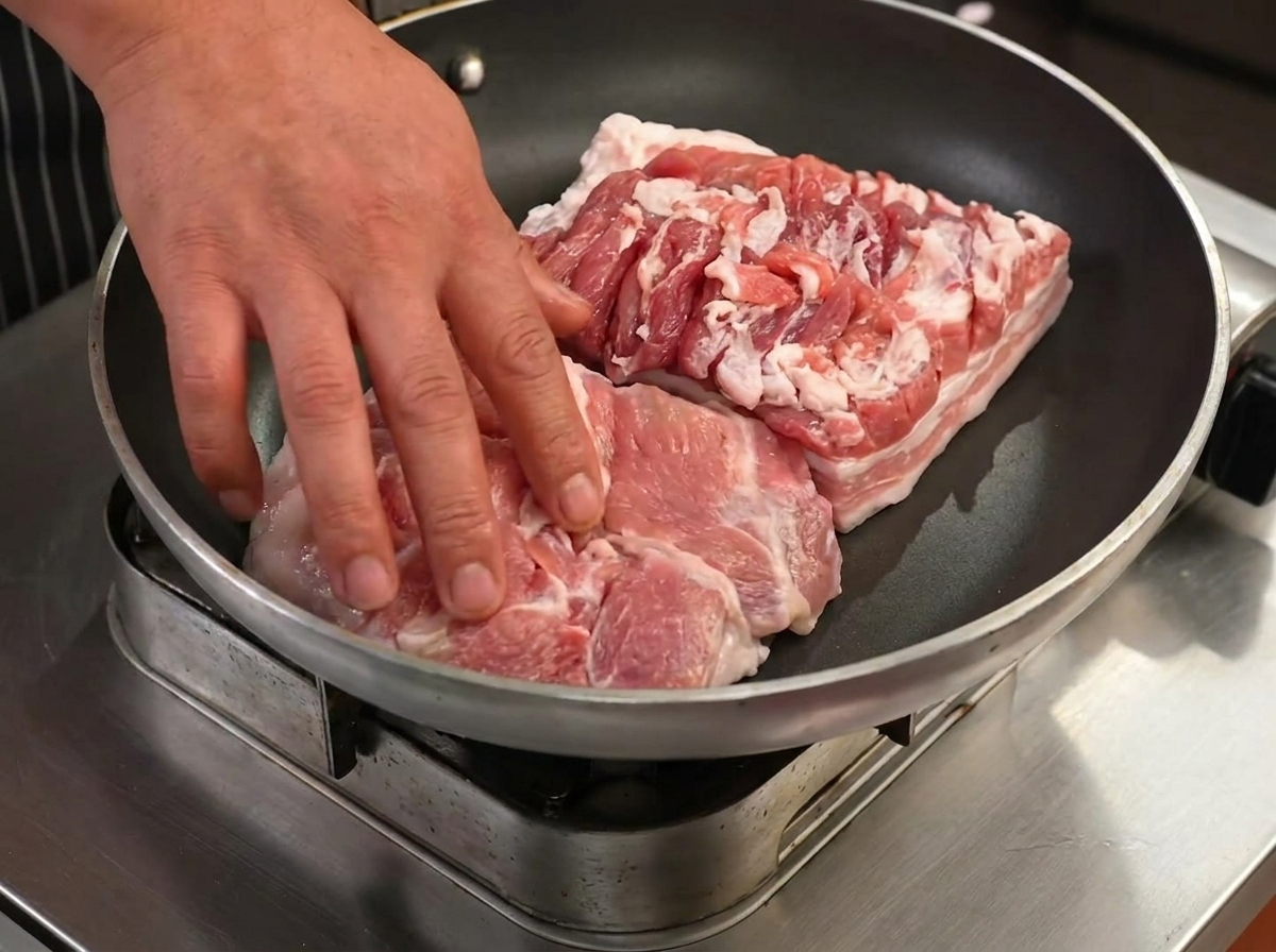 Slices of pork belly frying in a dry pan, beginning to brown and render their fat.
