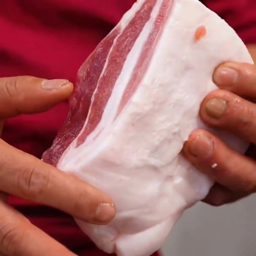 Pork belly held in hands, showing the cross-hatch cuts made at a 45-degree angle.