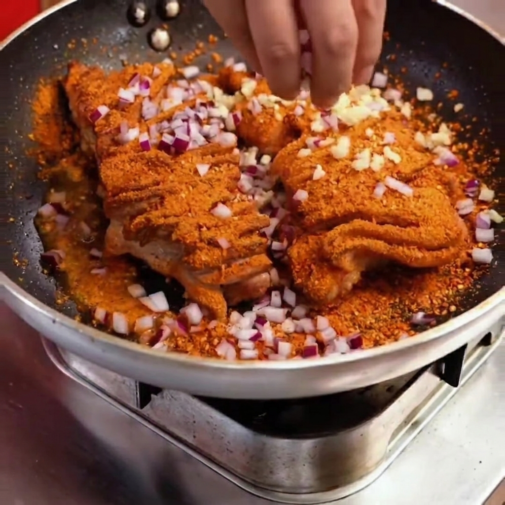 Close-up of diced red onion and green peppers being added over the spiced pork in the pan.
