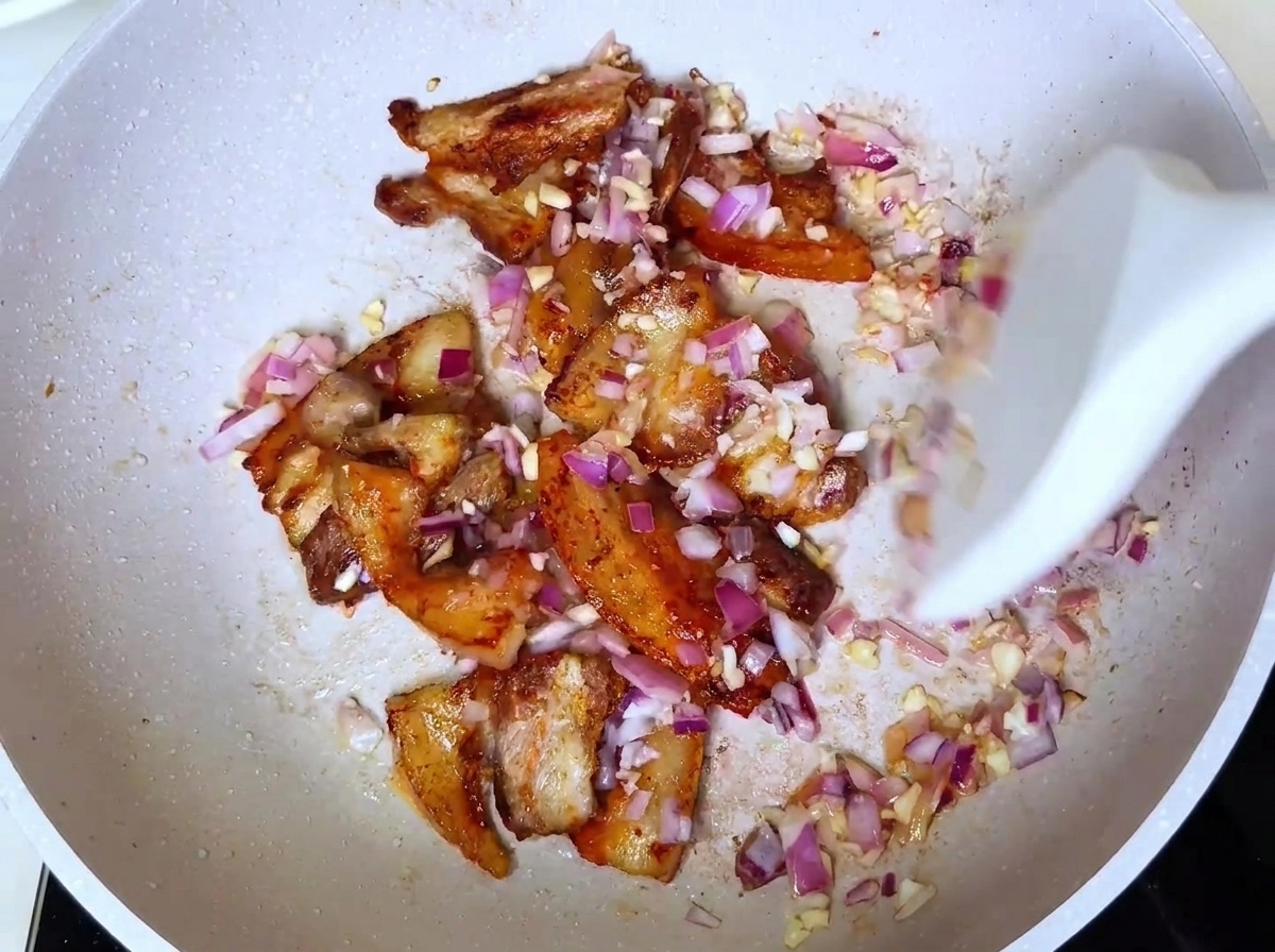 A white spatula stirring pork and diced onions in a pan after adding barbecue seasoning.