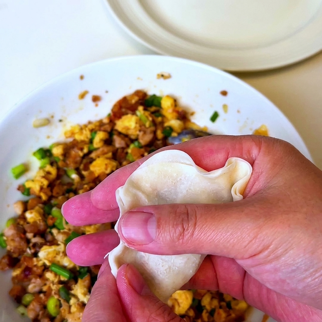 A hand holding a dumpling wrapper filled with the barbecue pork mixture and folding it shut.