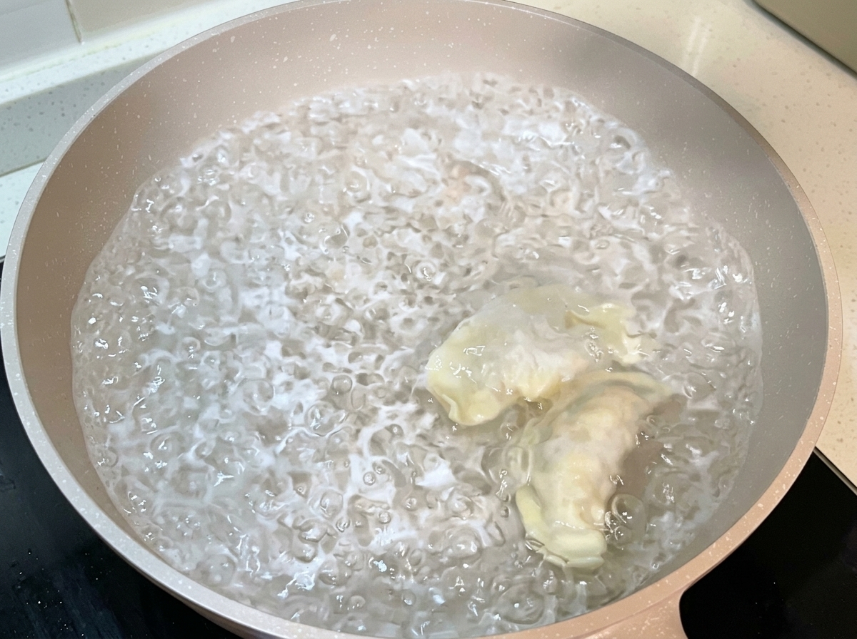 Wrapped dumplings being dropped into a large pan of boiling water.
