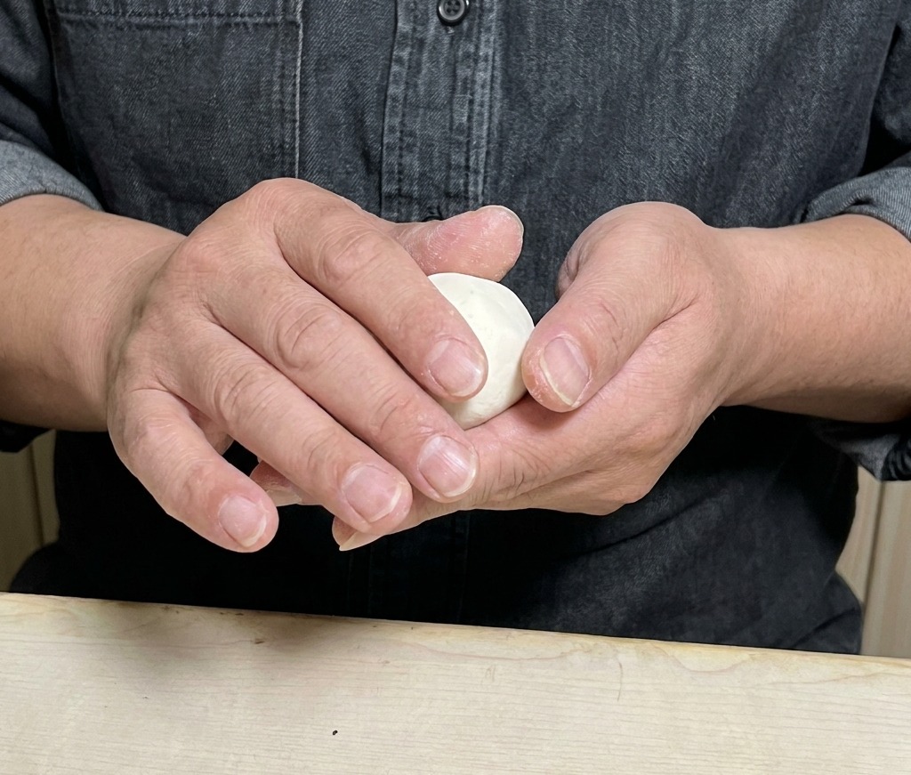 Hands carefully folding and sealing a round dough wrapper filled with meat mixture.