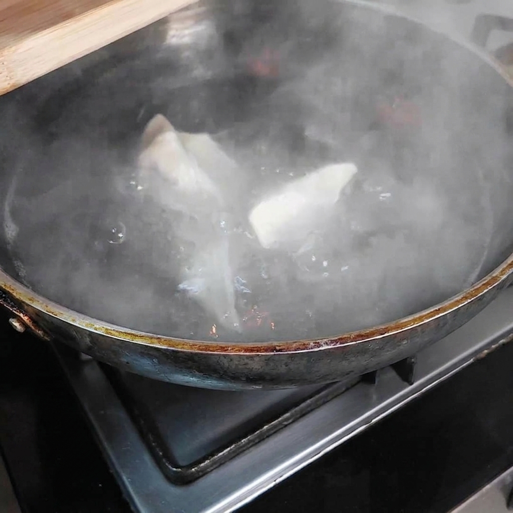 Several dumplings submerged in a large pot of boiling water, with steam rising from the pot.