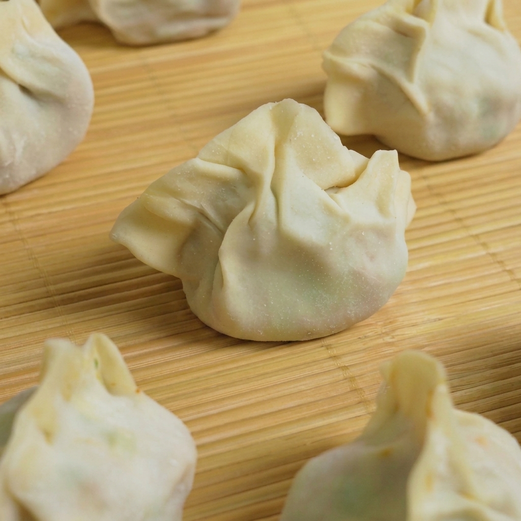 Several prepared dumplings being dropped into a pot of boiling water for cooking.