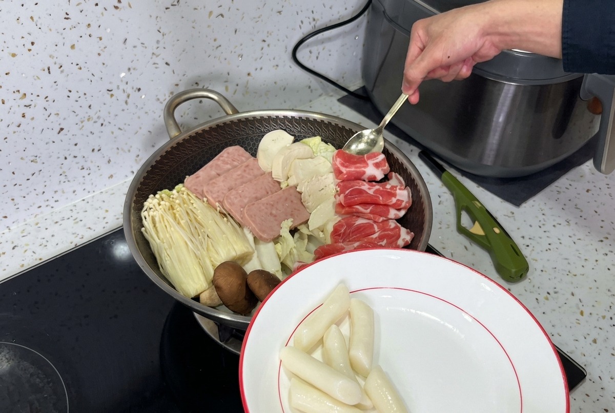 A beautifully arranged pot of Korean Army Stew, with layers of luncheon meat, mushrooms, tofu, and fresh kimchi ready for the broth.