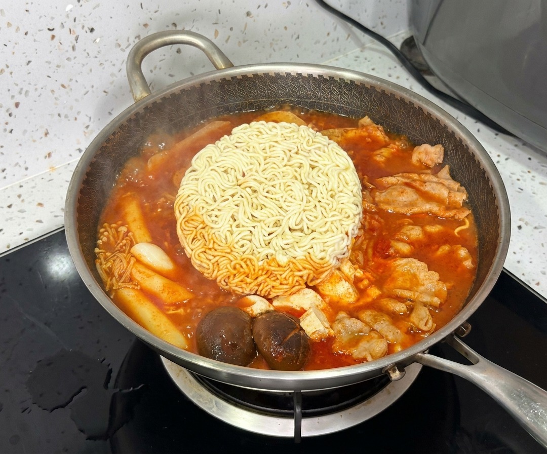 A block of ramen noodles cooking in the center of the vibrant, bubbling Korean Army Stew.