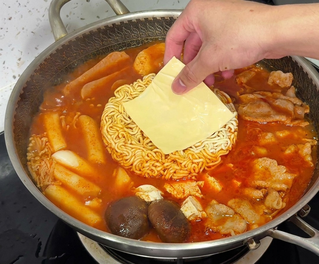 A slice of yellow cheese melting over the ramen noodles in a steaming pot of Budae Jjigae.