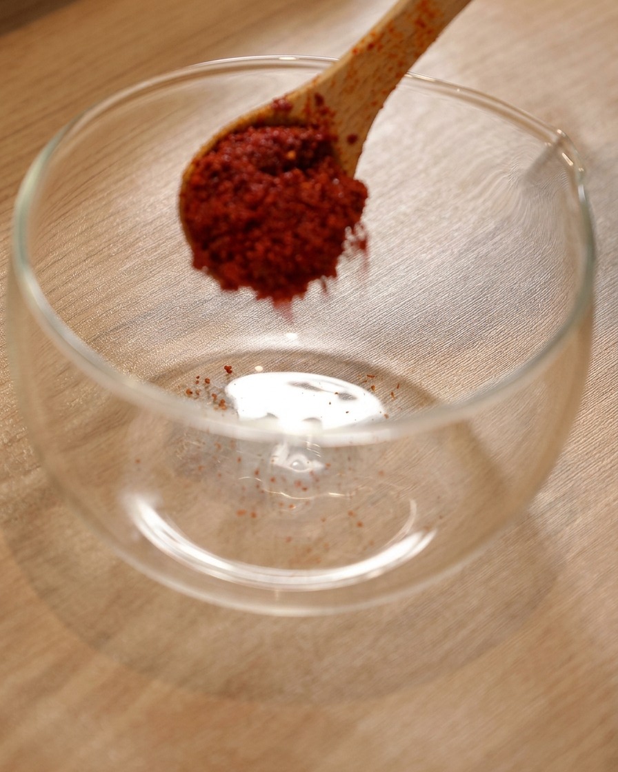 Chili powder in a glass bowl with Korean hot sauce and light soy sauce being added.