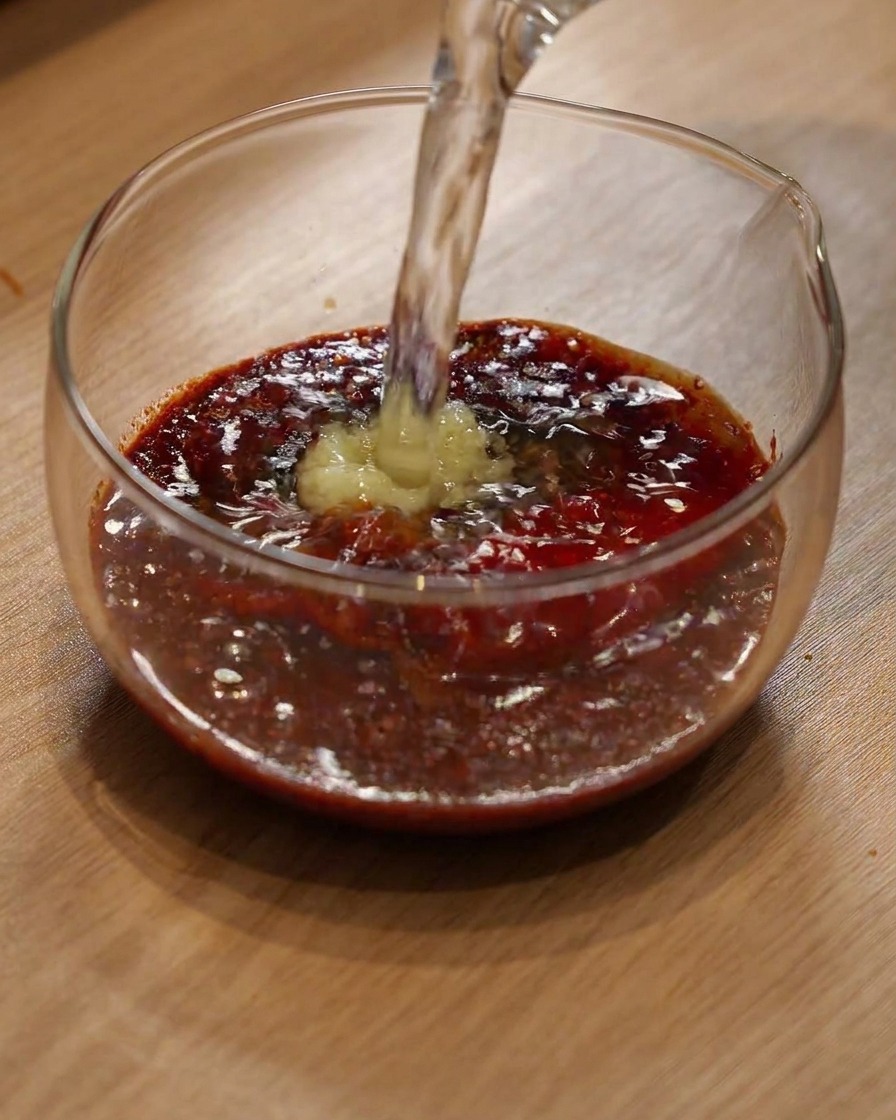 Water being poured into a glass bowl with chili powder and seasonings.