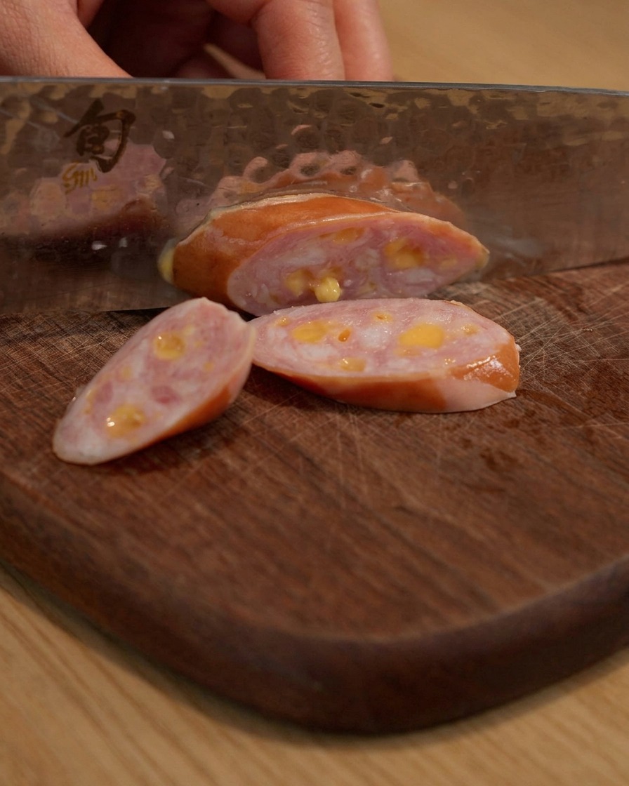 Sausage being sliced on a wooden cutting board.