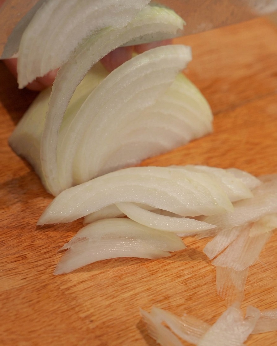 An onion being cut into shreds on a wooden cutting board.